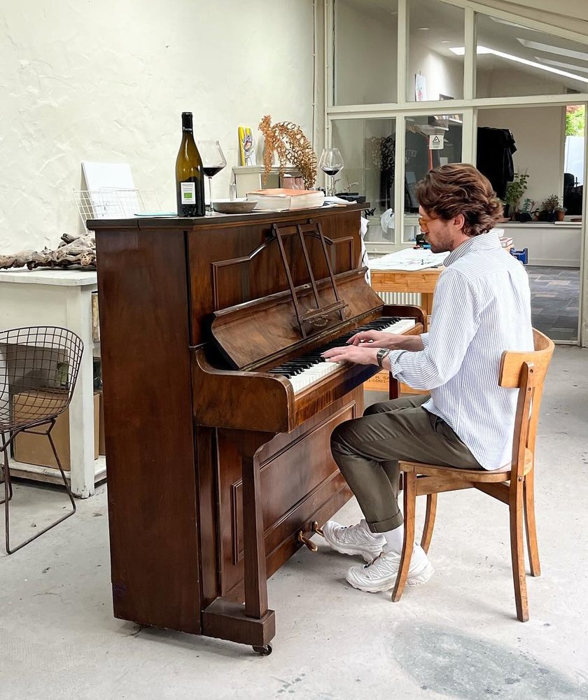 Alex playing an upright piano in a sunlit studio